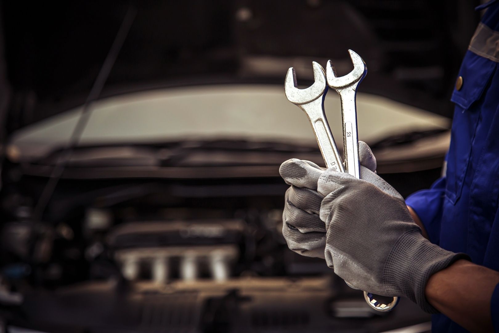 Mechaniker mit zwei Schraubenschlüsseln vor unscharfem Motorraum